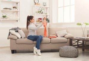 Woman folding clean t-shirts, sitting on sofa at home.